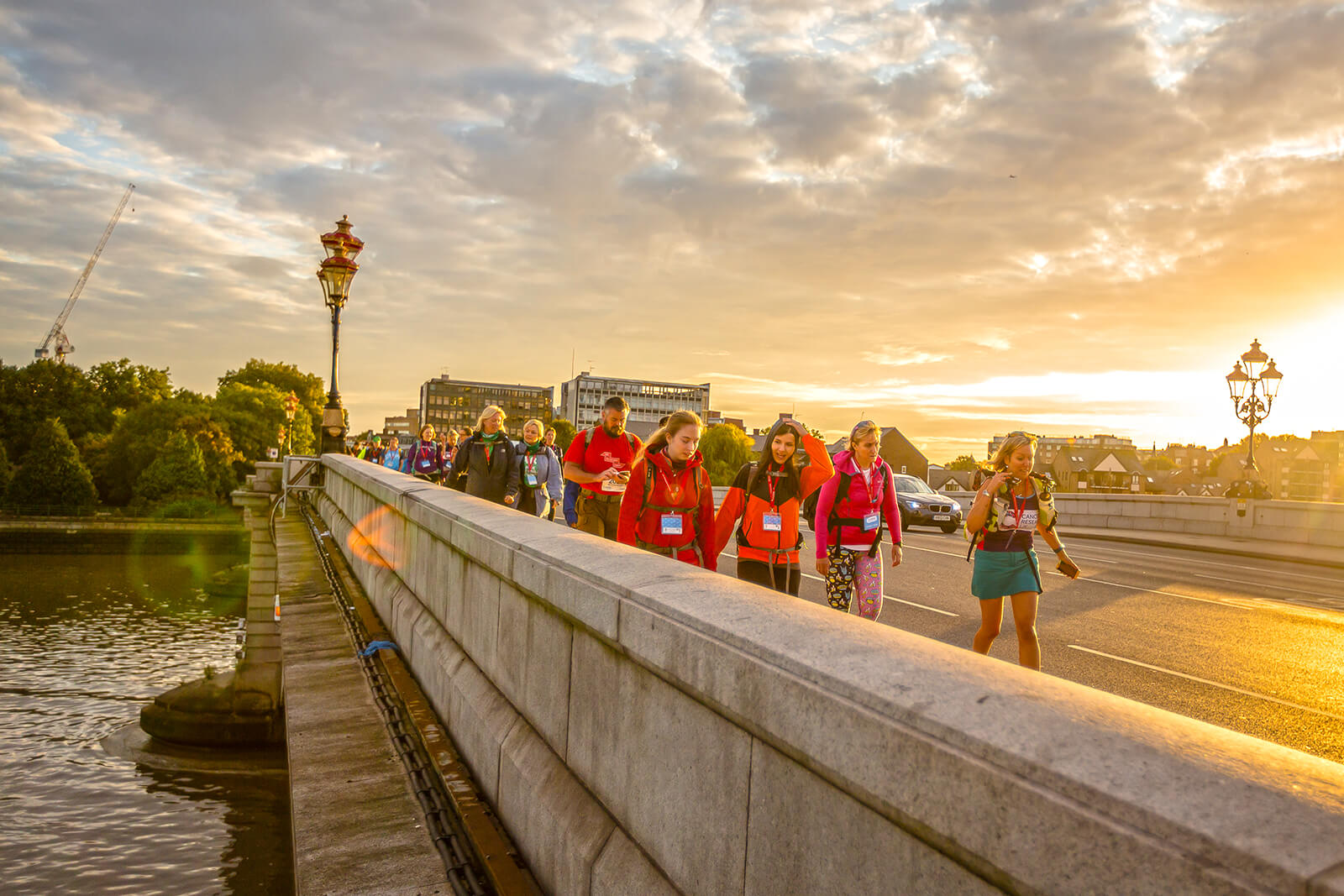 A group of people walking across a bridge at sunset.