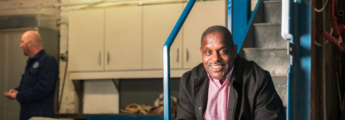 A photo of Errol who was diagnosed with prostate cancer in 2010. He is sat down on a staircase and appears to be in a car garage.