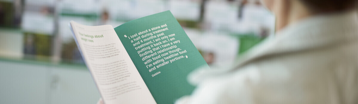 A patient reads a booklet produced by Macmillan in a Macmillan Support Centre. In the background you can see a shelf of other booklets. 