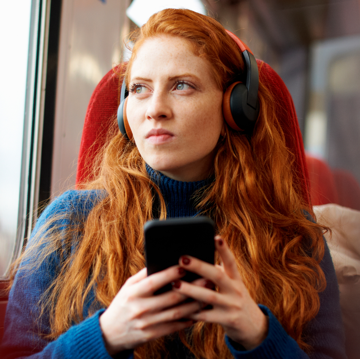 A woman on the train holding her phone and looking out the window