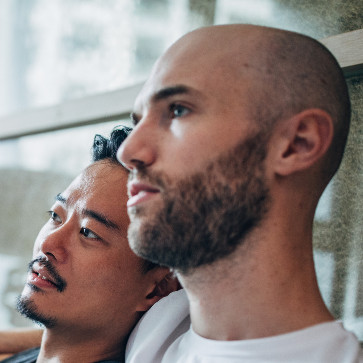 Two men sitting on a sofa watching tv. One has his arm around the other's shoulder.
