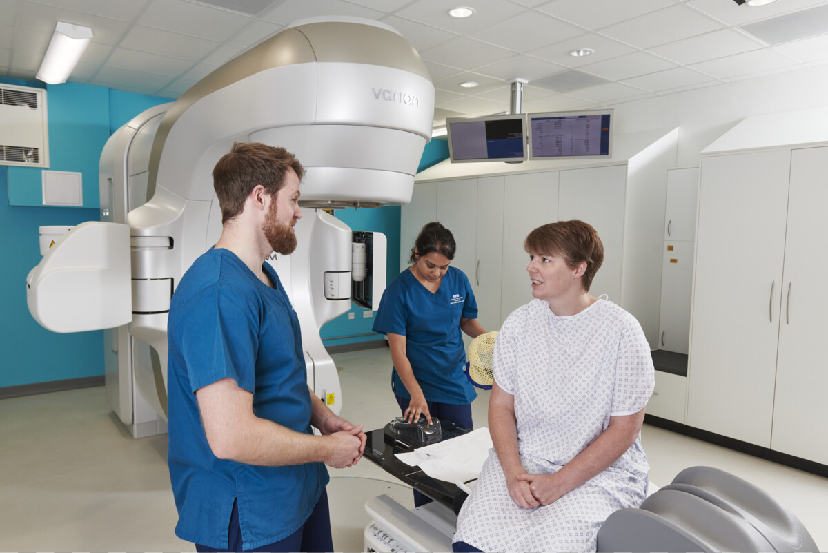 Patient in radiotherapy room talks to nurses