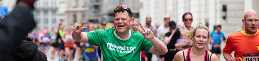 Man smiling and posing for phone in green Macmillan t-shirt, while taking part in marathon.