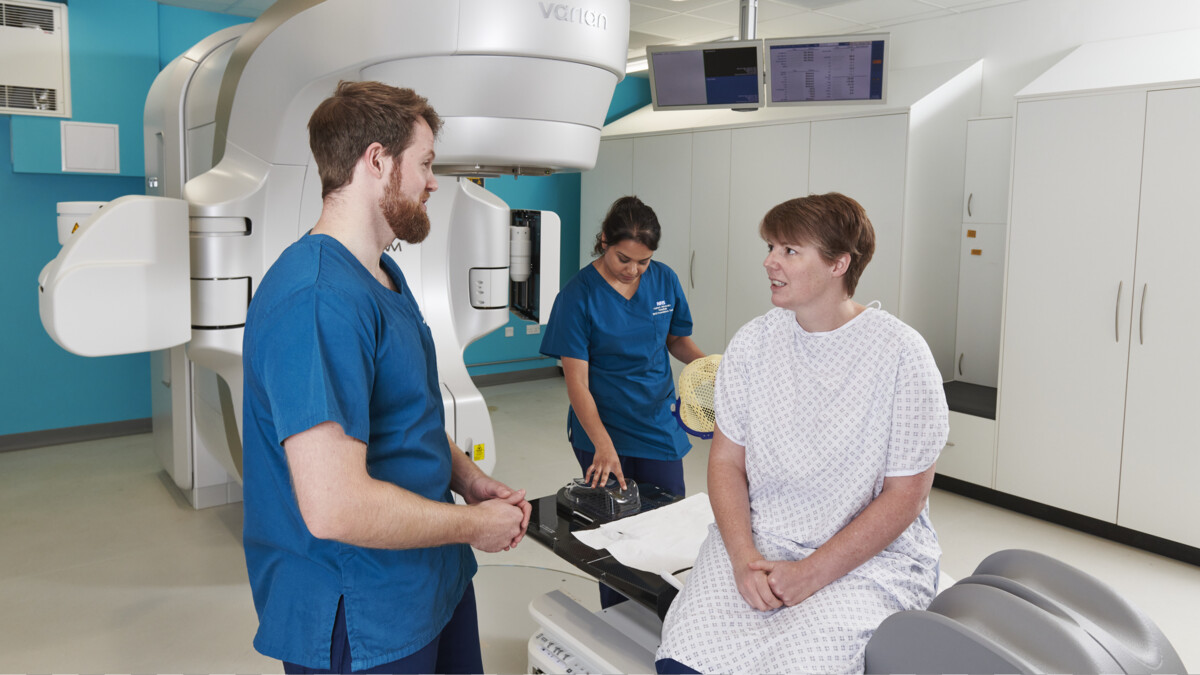 Patient in radiotherapy room talks to nurses