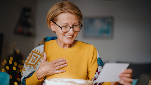 Woman wearing yellow top smiling at a card.