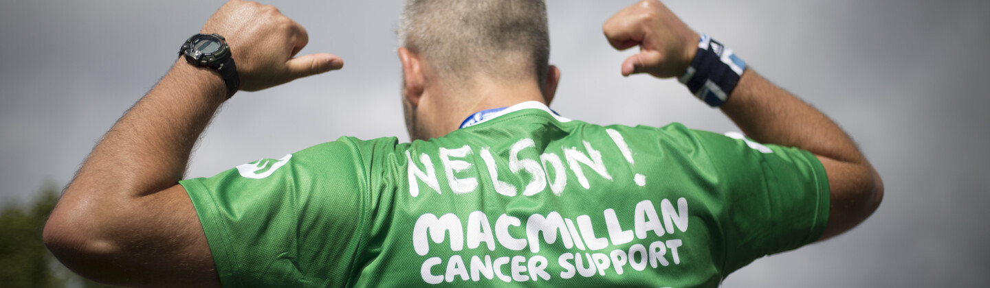 A male runner points at the back of his Macmillan running shirt at Edinburgh Marathon