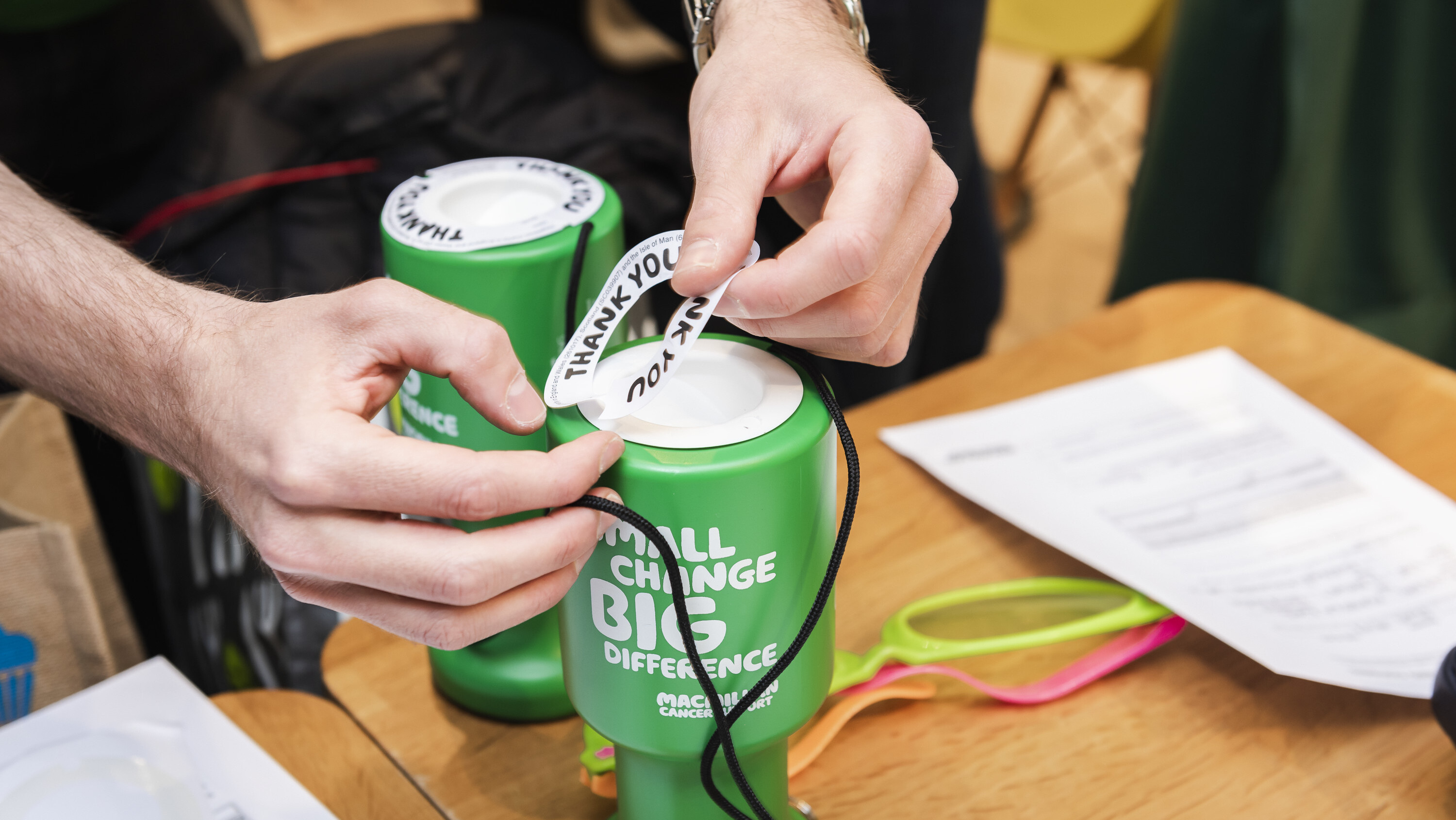  close-up of a man's hands sticking labels on the top of a Macmillan collection tin