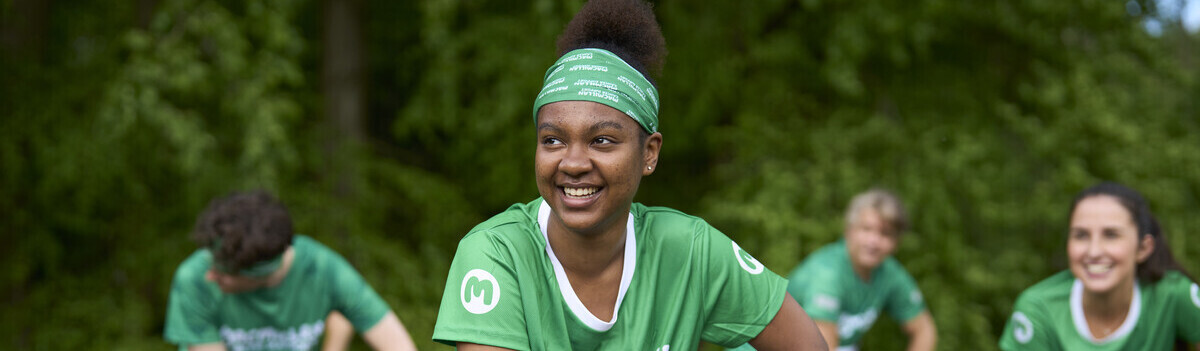 A group of people wearing Macmillan tops are seen outside stretching. They are leaning to one side and their arms are placed on one leg.