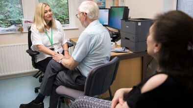 A female practice nurse in a white shirt is with an older patient, a man in a blue shirt.