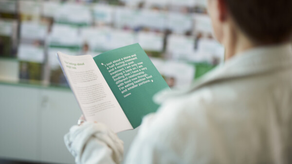 A patient reads a booklet produced by Macmillan in a Macmillan Support Centre. In the background you can see a shelf of other booklets. 