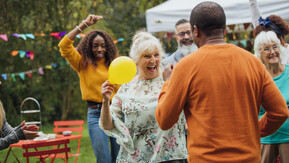 A woman smiles and dances with a man in garden. There are other people dancing in the background and there is bunting hanging.