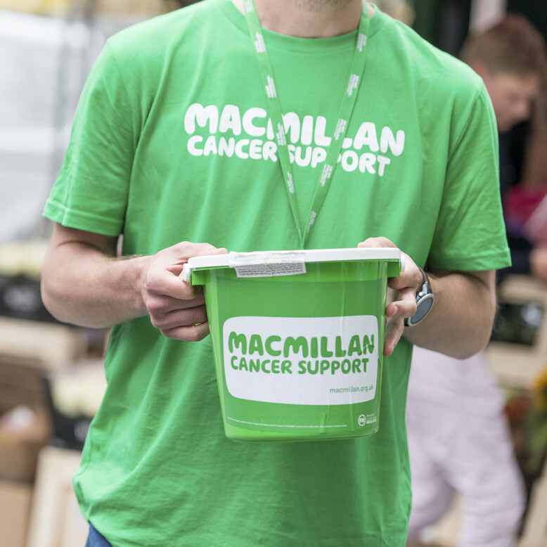 A person wearing a Macmillan t-shirt holding a fundraising bucket