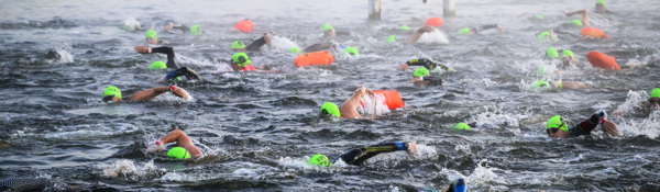A group of swimmers in florescent swimming caps. The image only shows the heads of the swimmers and their arms. They are in a body of water. 
