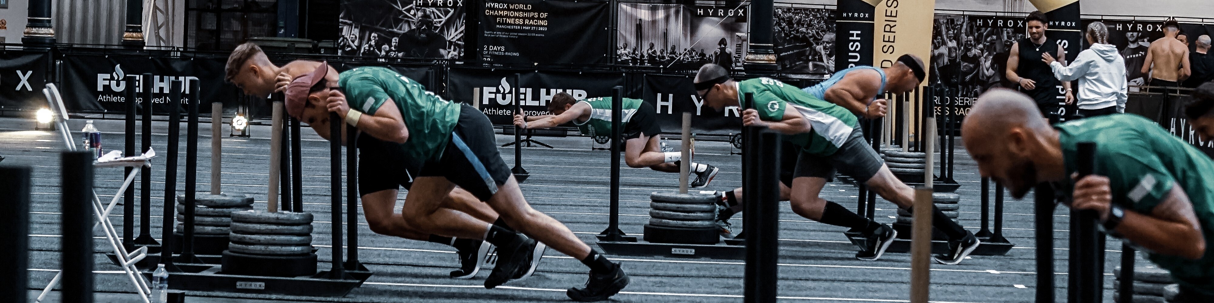Racers in Macmillan shirts doing sled pushes