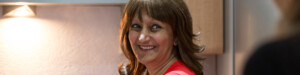 Woman in red top smiling while standing in a kitchen.