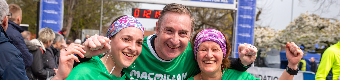A man and 2 women stand together smiling at the finish line of a race.