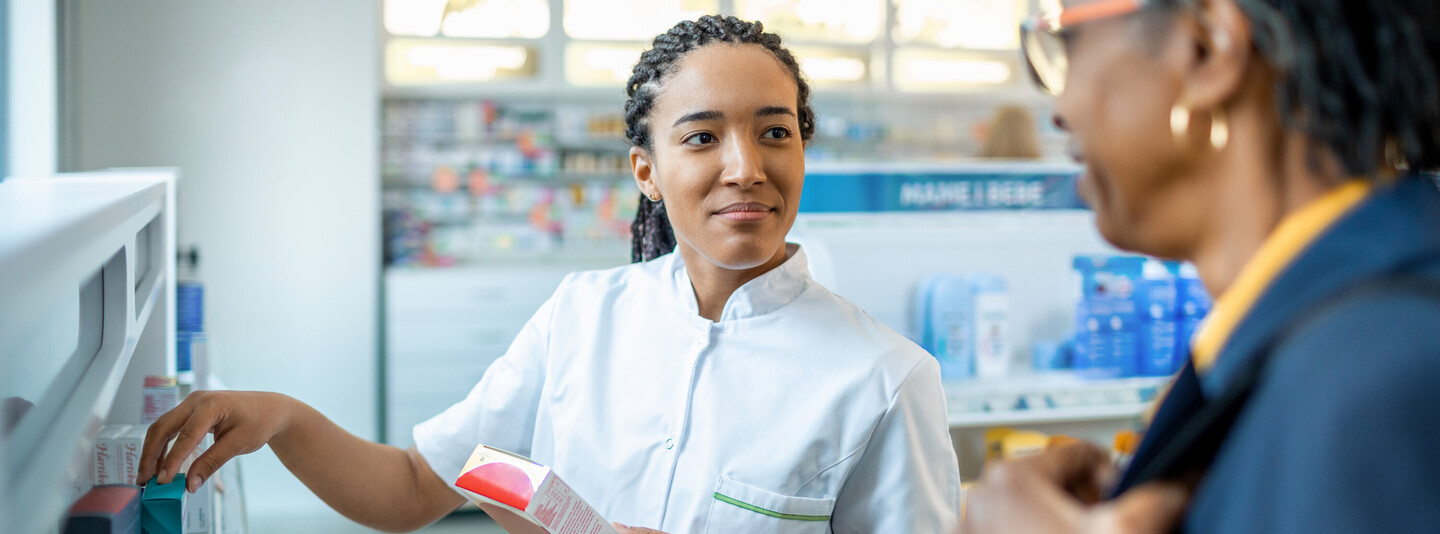 A pharmacist talking to someone about the medications on a shelf.