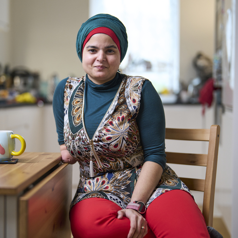 Woman sitting at kitchen table smiling while looking at camera.