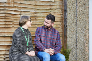 Man in checked shirt talking to Macmillan employee while sitting outdoors