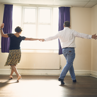 Two people dancing. They are holding hands and facing away from the camera.