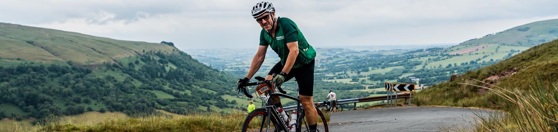 Man riding up a steep road wearing a Macmillan cycling top