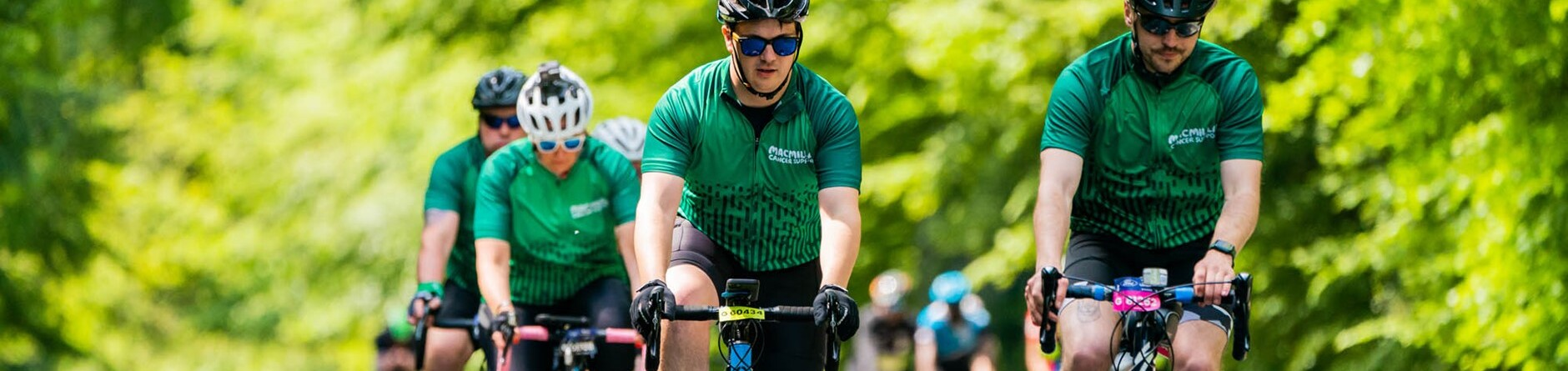 A group of cyclists all wearing green Macmillan cycling jerseys