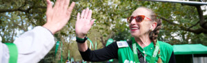 A person in red sunglasses and a green Macmillan top is high fiving another person. They appear to be on a path at an event. 