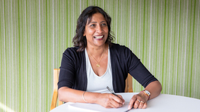 A woman sitting at a table with a notepad smiling