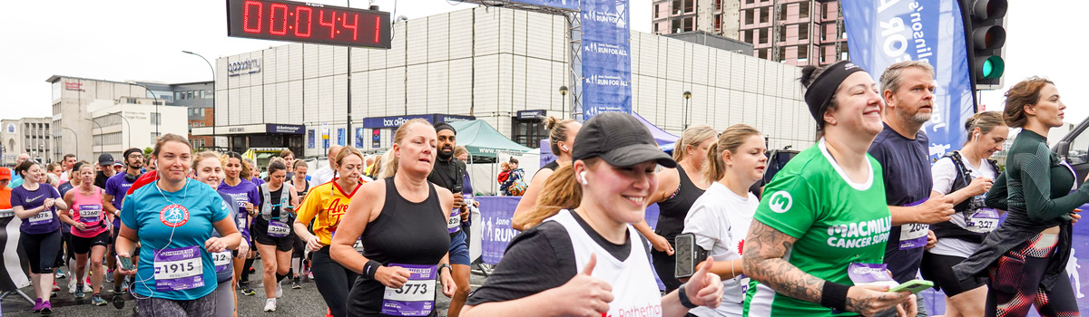 A group of people running past a starting line at an event. They are wearing different running clothes. 