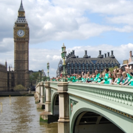 Lots of people all dressed in  green Macmillan tops standing on Westminster Bridge in London with Big Ben in the background