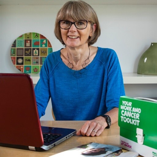 A woman sitting at her laptop with the Macmillan cancer toolkit on her table