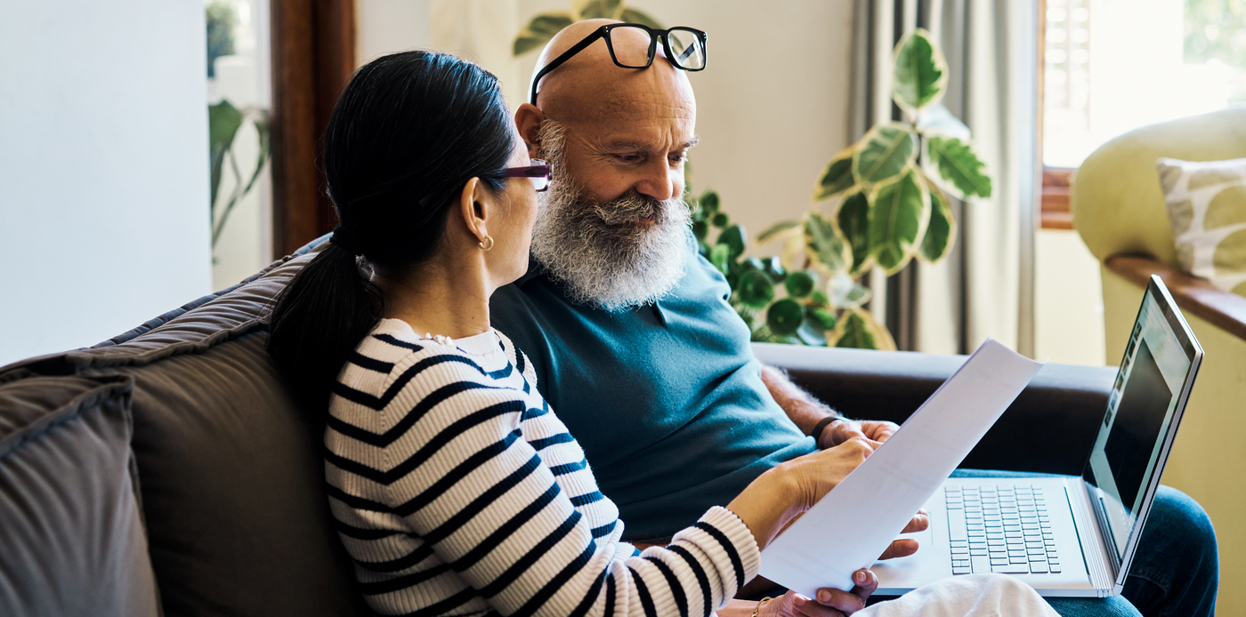A bearded man and a woman sit on a couch together with a laptop