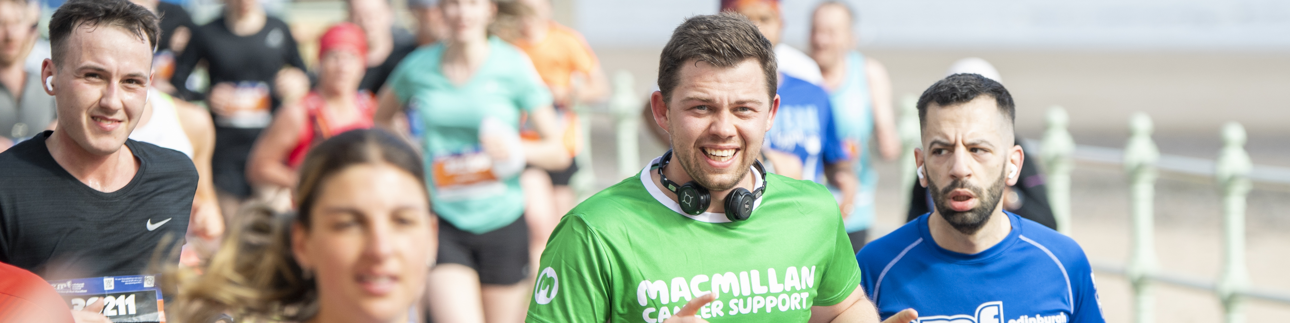 Man surrounded by other runners in a Macmillan running t-shirt