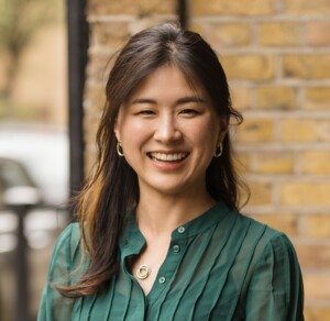 Woman with long brown hair smiling at camera, she is wearing a green shirt.