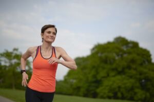 Woman running outdoors. She has short brown hair and is wearing an orange vest.
