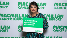 A south Asian lady with brown hair with a sign supporting people with cancer .