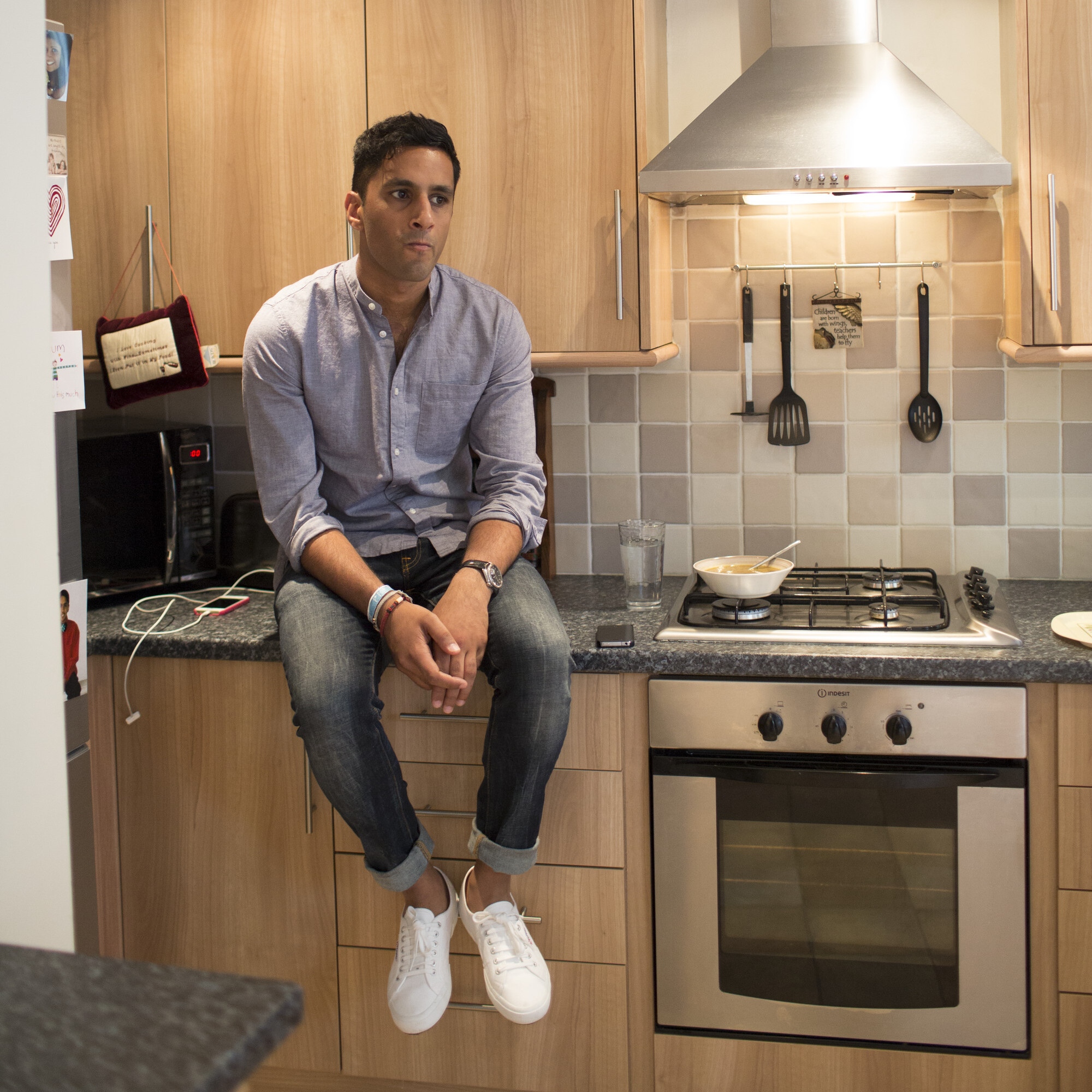Amrik, a young person diagnosed with cancer, sits on the kitchen counter in his home