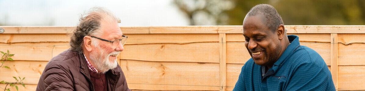 Two men sitting across from each other on a picnic bench talking.