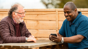 Two men sitting across from each other on a picnic bench talking.
