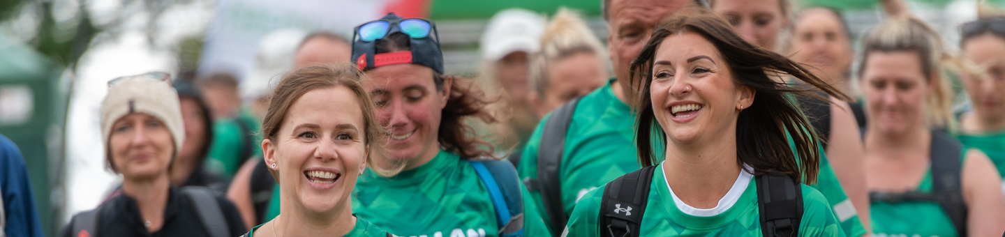 Two smiling women walking along in  crowd of other walkers, wearing green Macmillan t-shirts