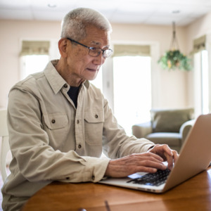 A photo of a man sitting at a table using a laptop.