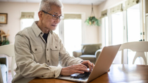 A photo of a man sitting at a table using a laptop.