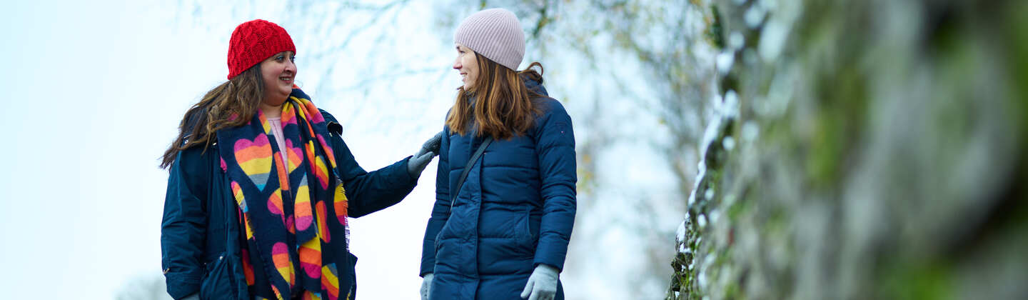 Two women walking in the cold. One has her hand on the other's shoulder