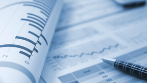 A close up view of a series of documents that contain different figures and data. There is a pen on one sheet of paper. 