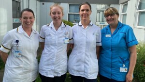 Four Allied Health Professionals are standing next to each other outside a hospital. Helen Scharf is on the left, next to her is Lauren Margery. Next to Lauren is Angela Jiggins and to the right is Tanya Bowers. They are all wearing NHS uniforms. 