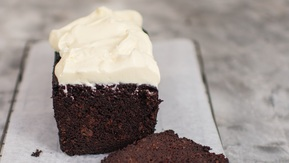 A chocolate cake with frosting on a cooling rack