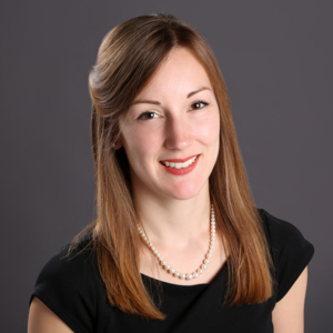 Dr Alison Berner has long brown hair. She is wearing a black top and a white pearl necklace. The photo shows her from the shoulder up. 