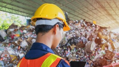 Someone at a recycling plant wearing a hi vis jacket and a hard hat