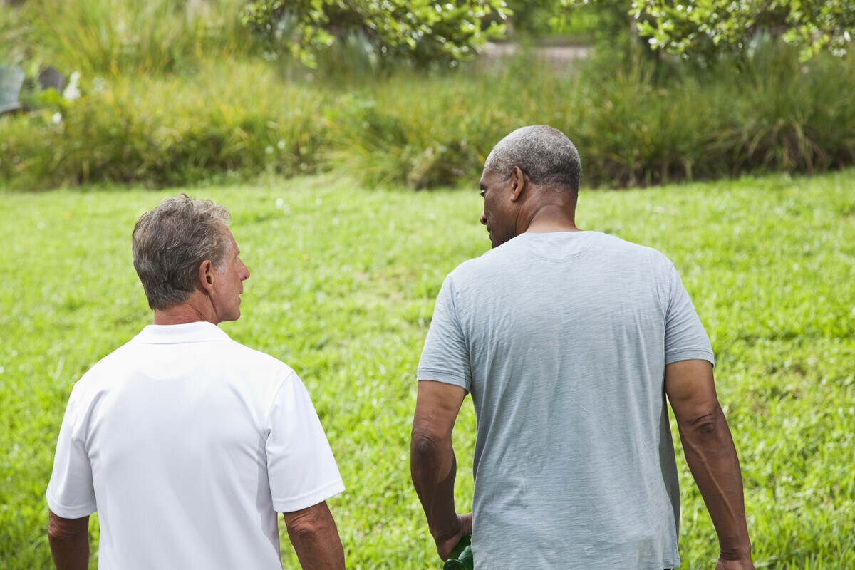 Two men in conversation walking outdoors. They both have their back towards the camera.
