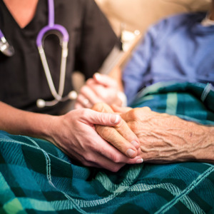 A medical professional sits holding a patient's hand